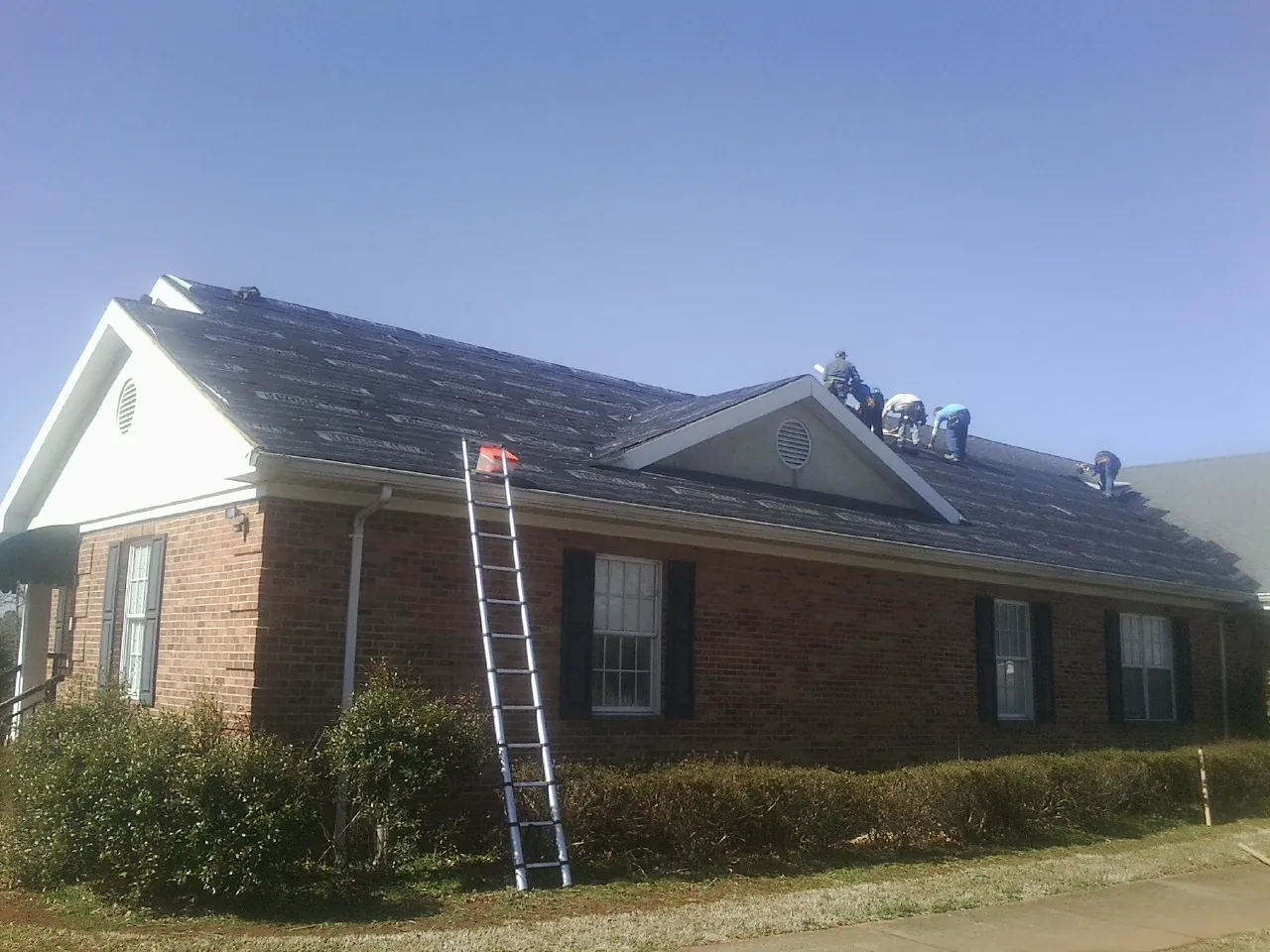 Crew tearing shingles off a brick ranch roof with a ladder set — Metal Roof Repair work by our crew in Vina