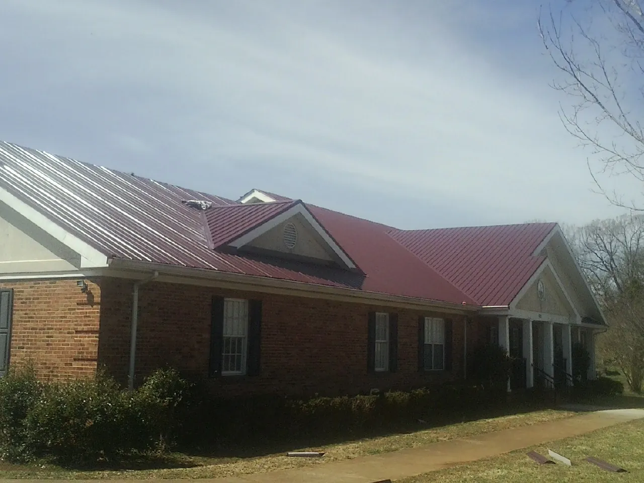 Red metal roof with gabled entries on a long brick building, from a Hail Damage Roof Repair job in Vina