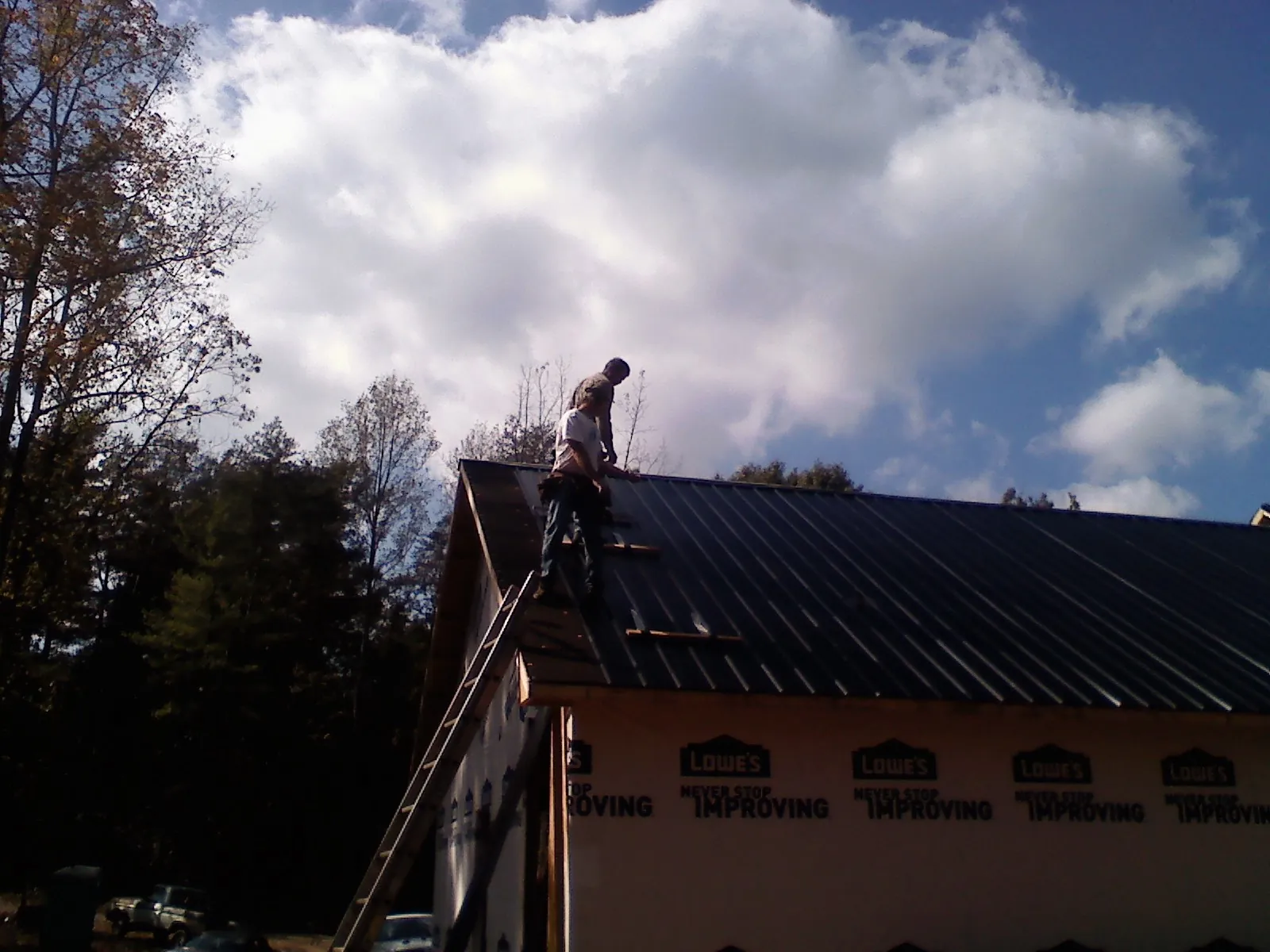 Roofer fastening dark metal panels high against a cloudy sky, from a Roof Inspection job in Vina