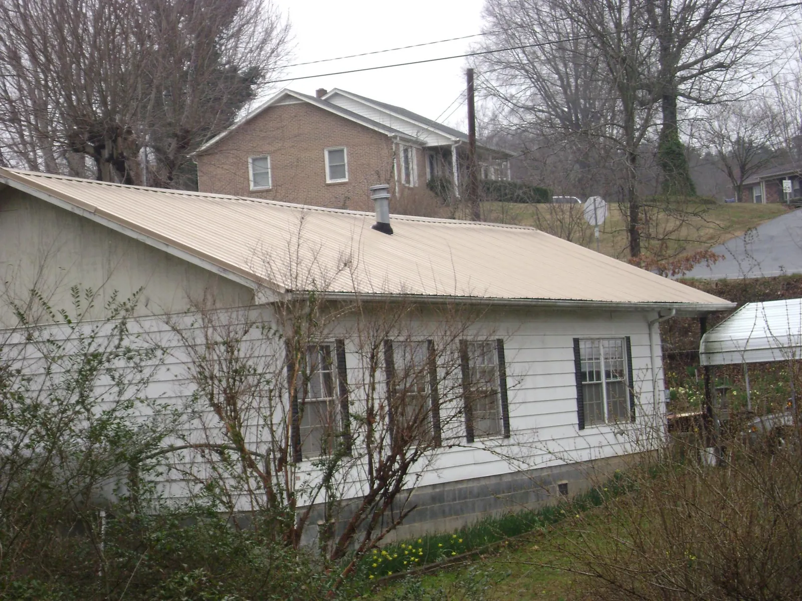 Tan metal roof on a white sided house set into a hillside — Commercial Roofing by Roofing Brothers in Vina